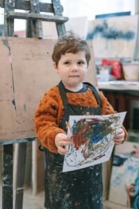 A young child displaying colorful artwork in an art classroom.
